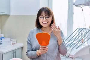 A woman looking in a mirror smiling at her dental office